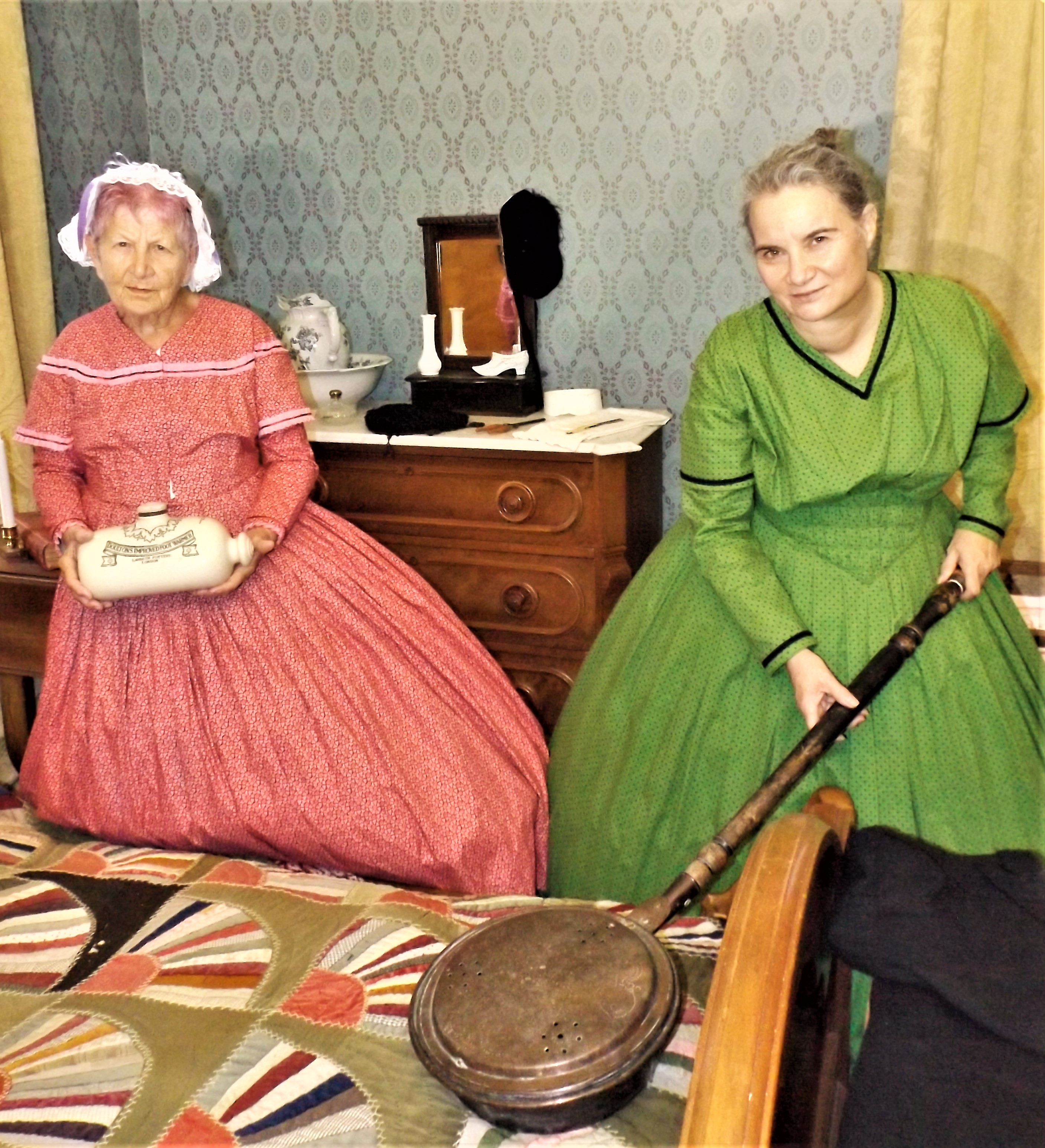 Two women in Victorian dress demonstrate historical artifacts.